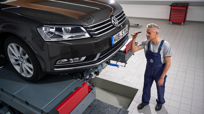 VW Passat B7 on lifting platform, VW service employee inspects bumper with lamp