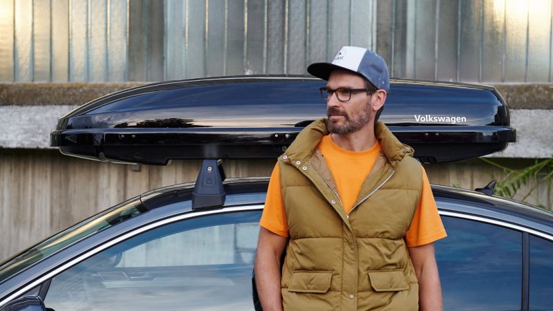 Man leaning against a VW Passat B8 with roof box – accessories for previous models