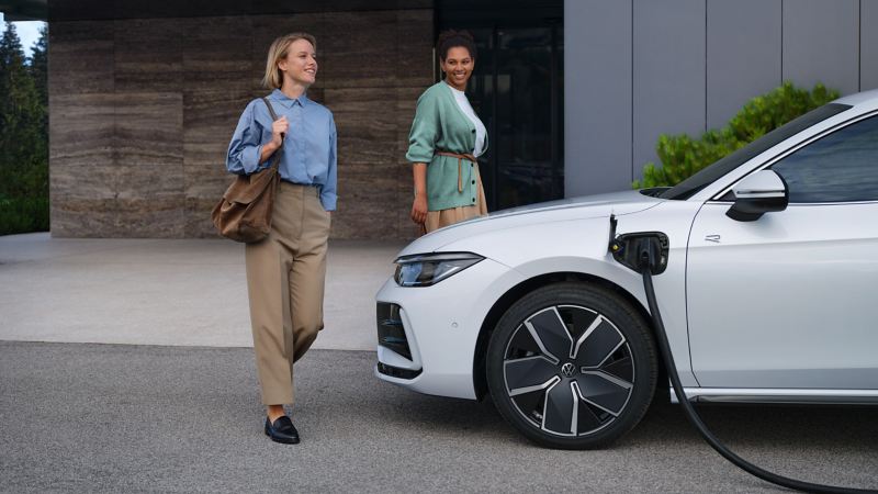 Two women next to VW Passat model that is being charged