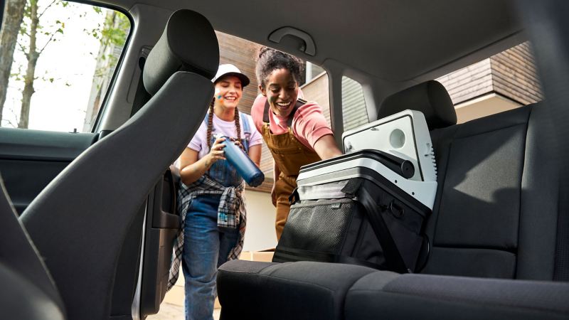 Two women filling VW Accessories cool and thermos box on the back seat of a VW car