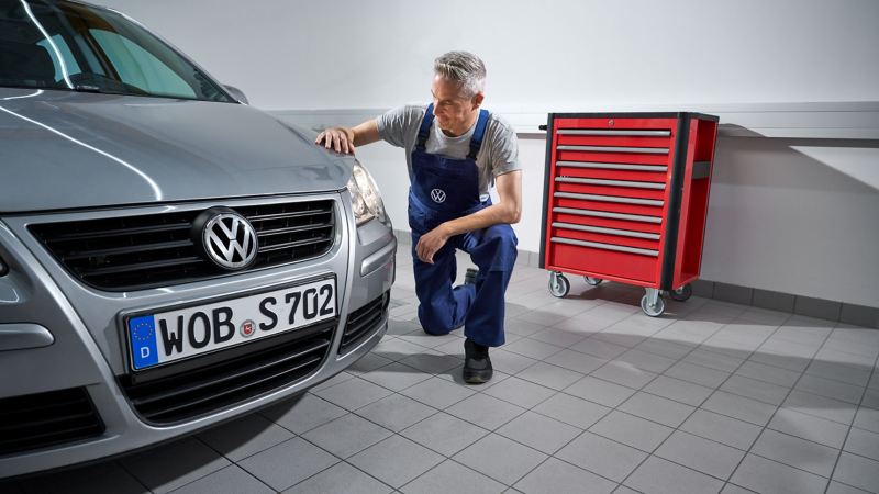 VW service employee kneels next to VW Polo 4 and looks at headlights