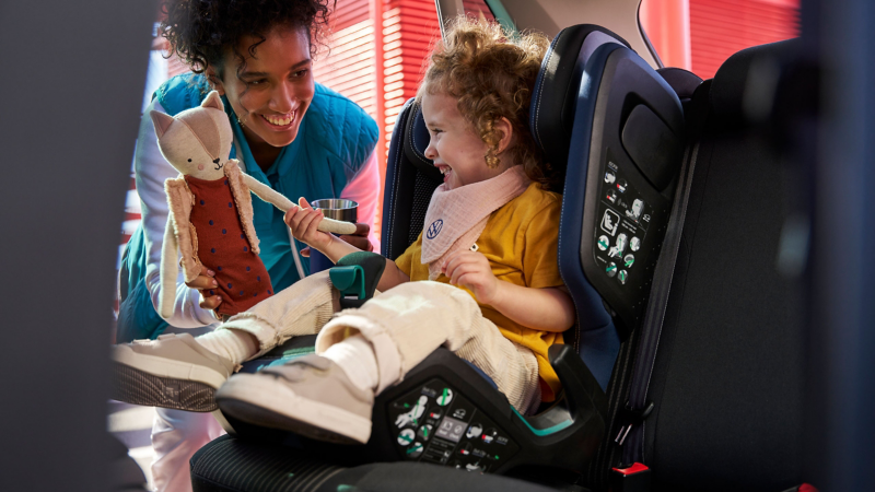Woman gives cuddly toy to child sitting in VW Accessories child seat – Accessories for previous models