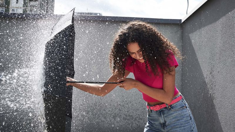 Eine Frau hält ihren Schirm schützend gegen eine Wasserfontäne