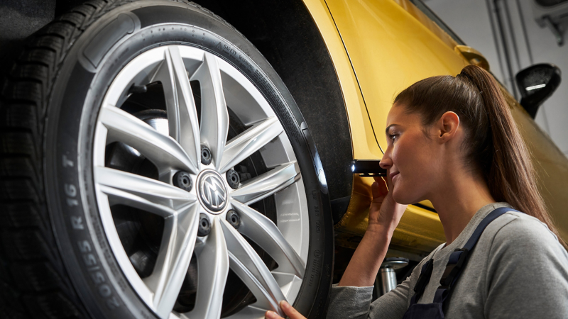 VW Servicemitarbeiterin inspiziert mit kleiner Taschenlampe einen VW Reifen – Reifenpakete