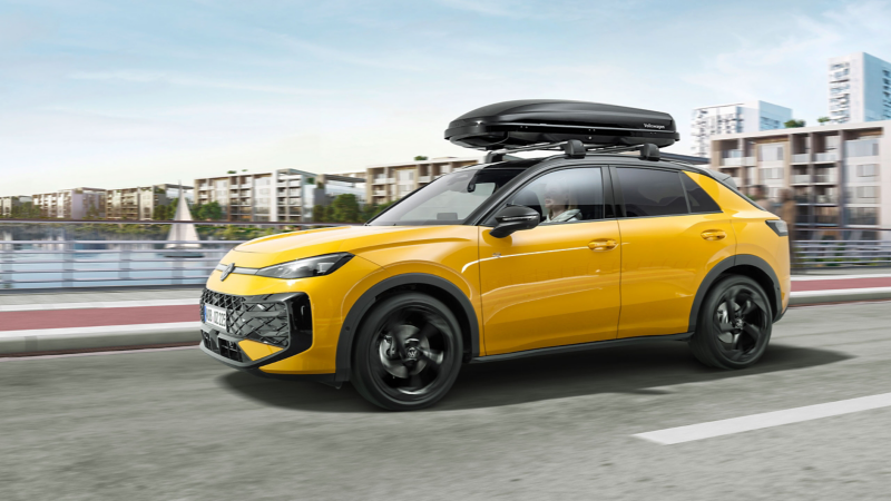 A yellow VW T-Roc with a roof box from VW Accessories driving along a road