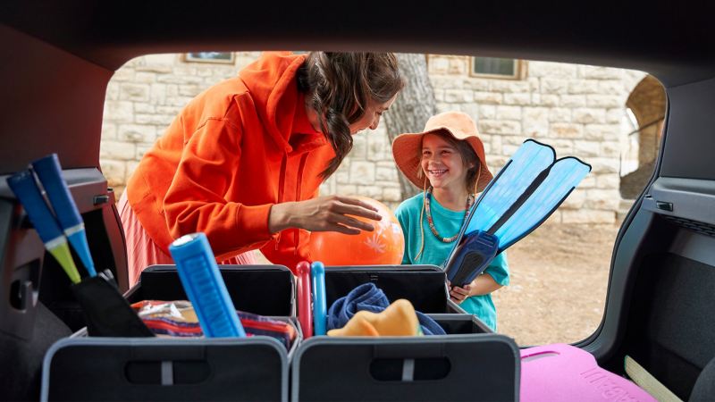 Blick aus dem Kofferraum eines Golf 8 GTI – Mutter und Sohn packen Strandsachen in eine Faltbox von Volkswagen Zubehör