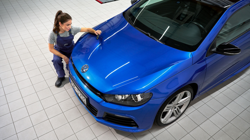 VW service employee inspects the paintwork on the bonnet of a VW Scirocco 3