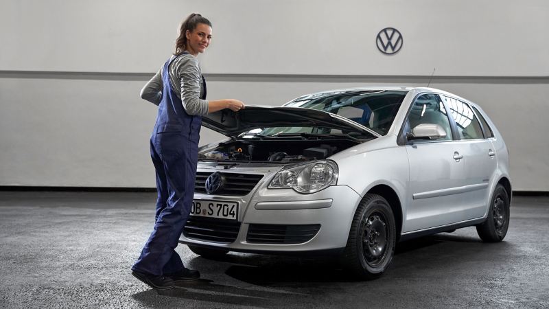 Eine VW Servicemitarbeiterin neben einem VW Polo mit offener Motorhaube