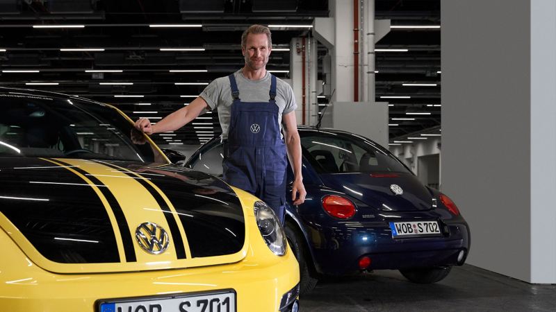 A VW service employee next to a New Beetle in the workshop
