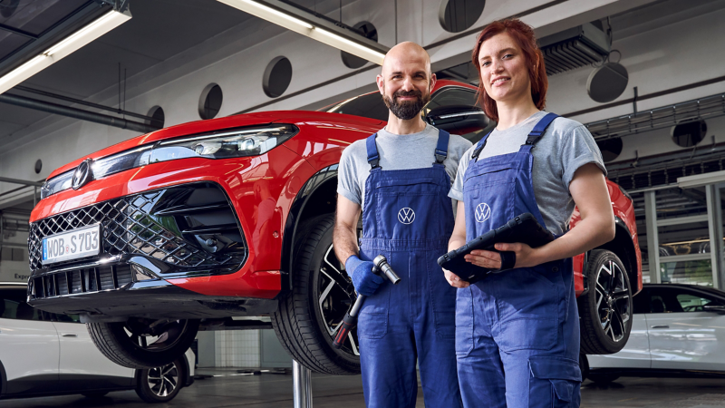 VW Servicemitarbeiterin und Servicemitarbeiter neben einem rotem VW Auto, das auf einer Hebebühne steht