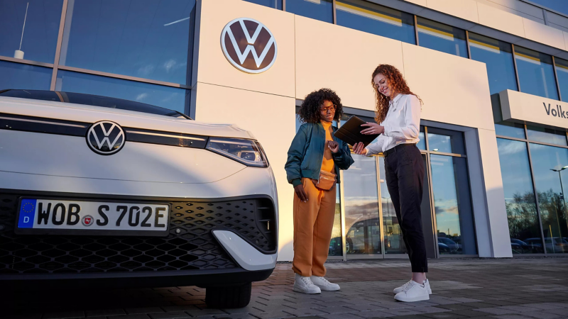 Volkswagen servicemedewerker laat iets zien aan klant op tablet, ze staan buiten een dealer locatie naast een ID. model