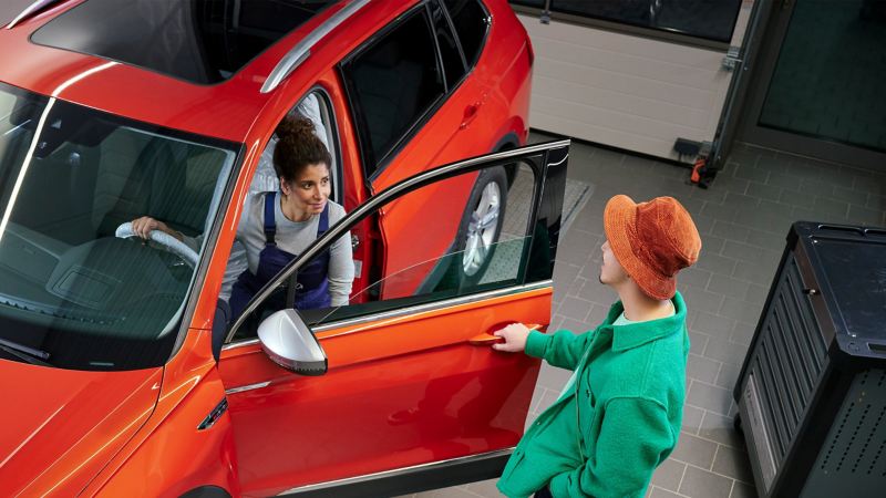 Eine Servicemitarbeiterin steigt nach dem Fahrzeug Check aus einem VW Tiguan, ein Kunde öffnet ihr die Tür