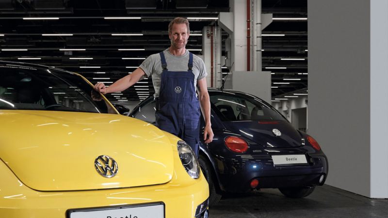 A VW service employee next to a New Beetle in the workshop