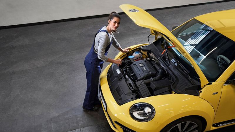 A VW service employee next to a Beetle with an open bonnet
