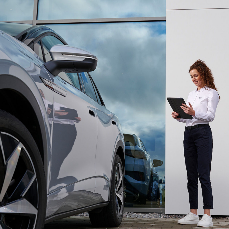 Frau steht neben einem Elektrofahrzeug von Volkswagen und blickt auf eine Tablet
