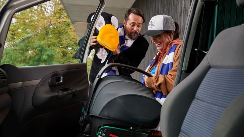 Woman takes baby carrier from VW car, man cheers up child with mascot – accessories for previous models