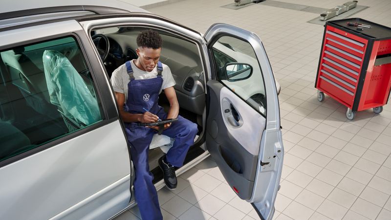 VW service employee sits in the passenger seat with the door open and writes something down on a tablet