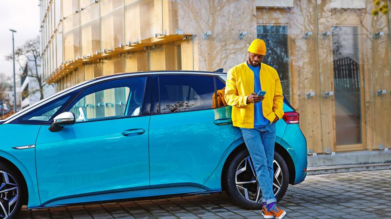 Ein Mann in einer gelben Jacke lehnt gegen seinen VW ID.