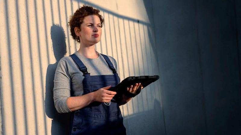 A service employee stands leaning against a wall with a tablet in her hand