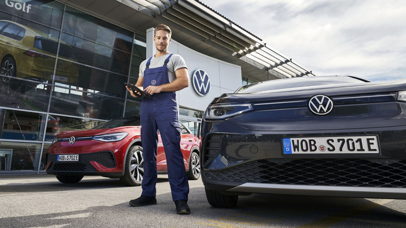 VW Servicemitarbeiter zwischen zwei VW Autos vor Werkstatt