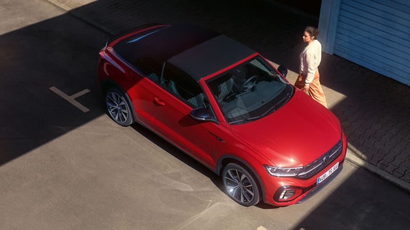 Eine Frau steht neben ihrem roten VW Cabriolet – Sommerreifen
