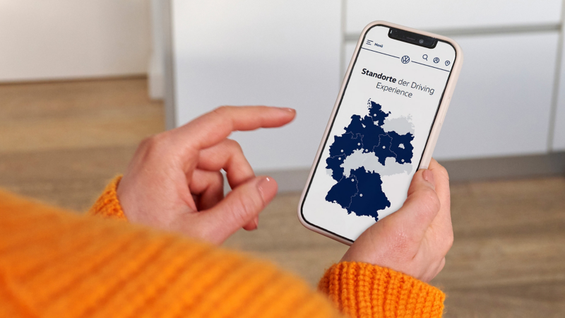 Jemand bedient Smartphone, auf dem eine Übersichtskarte mit VW Driving Experience Trainingsorten zu sehen ist
