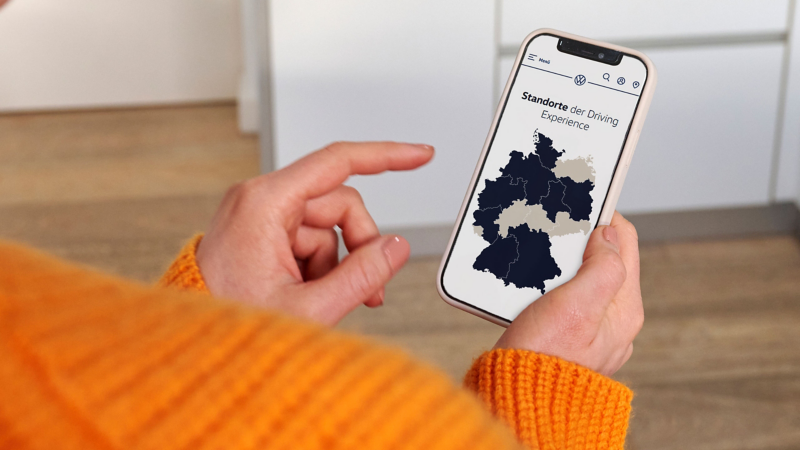 Jemand bedient Smartphone, auf dem eine Übersichtskarte mit VW Driving Experience Trainingsorten zu sehen ist