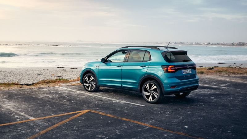 Een turquoise VW T-Cross op een parkeerplaats met uitzicht op zee