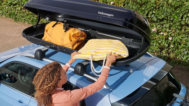 Een vrouw laadt de dakkoffer van VW-accessoires die bevestigd is op een VW T-Cross