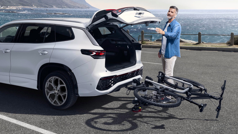 Άνδρας ανοίγει τον χώρο αποσκευών ενός Volkswagen Tayron, με αναδιπλωμένη τη βάση μεταφοράς ποδηλάτου, στον κοτσαδόρο, με  τοποθετημένο ποδήλατο