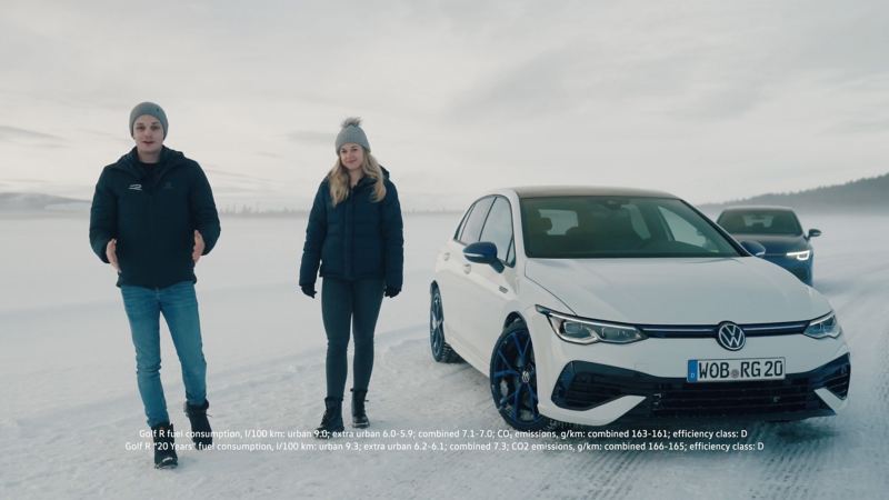Zwei VW R-Mitarbeiter stehen in einer Schneelandschaft vor dem weißen VW Golf R „20 Years“