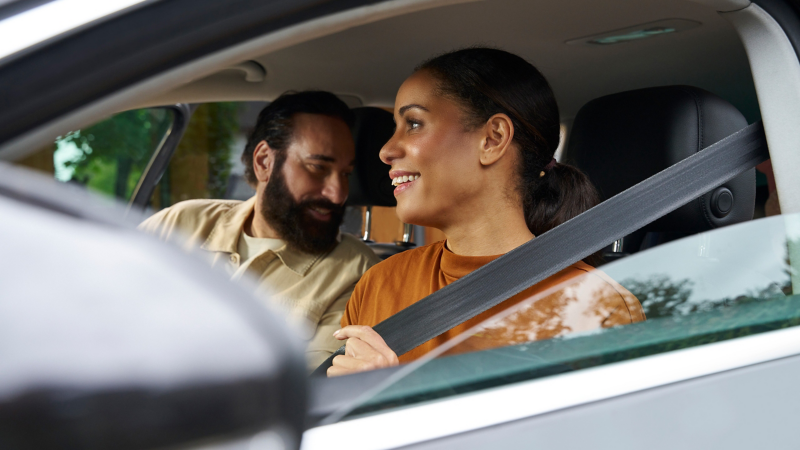 Frau in einem VW Auto schnallt sich an, bereit für eine VW Driving Experience, auf dem Beifahrersitz ein Mann