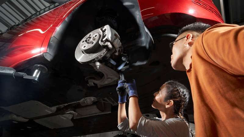 Véhicule VW sur une plateforme élévatrice, employée du service Entretien VW et client inspectant les freins ensemble