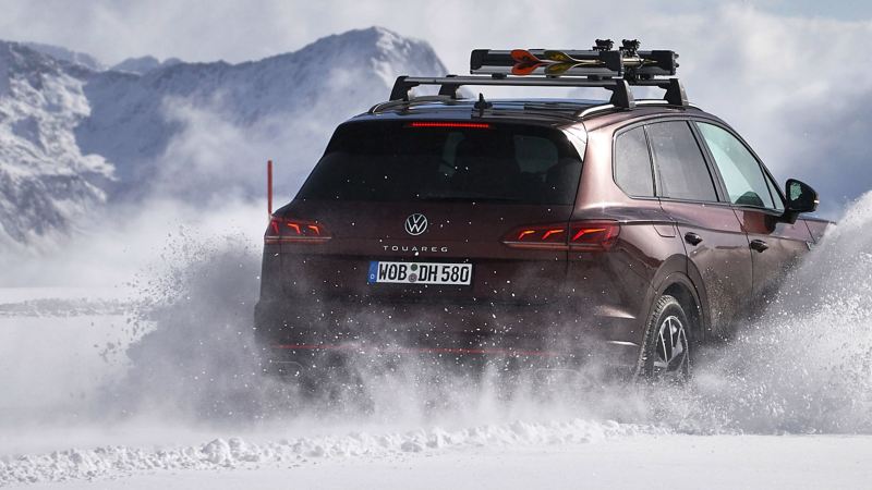 A VW Touareg drives on a snowy road and swirls up snow