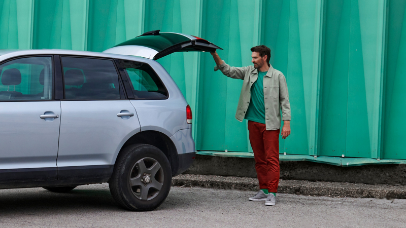 Man standing at open luggage compartment of a VW Touareg 1 in front of a green wall