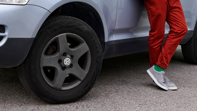 Close-up tyres incl. rim of a VW Touareg 1 and legs of a man leaning against the car