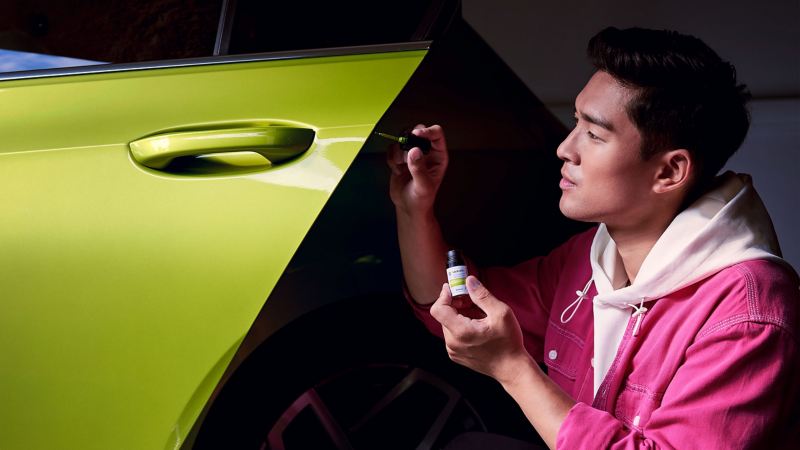 A man touches up a scratch with a VW touch-up pencil