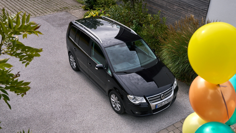 Man with smartphone in hand leaning against his VW MPV model