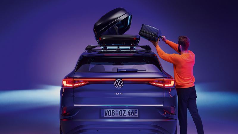 Ein Mann verstaut Gepäck in der VW Dachbox auf seinem VW ID.4