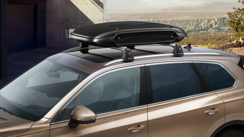 Une VW Touareg se gare devant une maison, elle présente des barres transversales sur lesquelles se trouve un coffre de toit des Accessoires VW