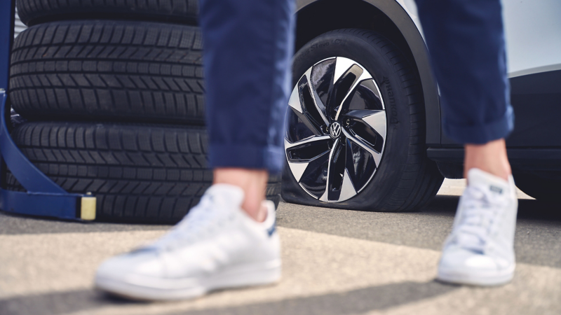 Nahaufnahme Füße einer Person, im Hintergrund gestapelte VW Räder und VW ID.4 Pro mit Rad im Fokus