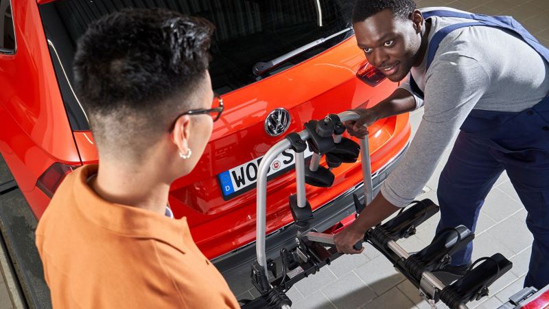 A VW service employee mounts a bicycle carrier on the VW for his customer