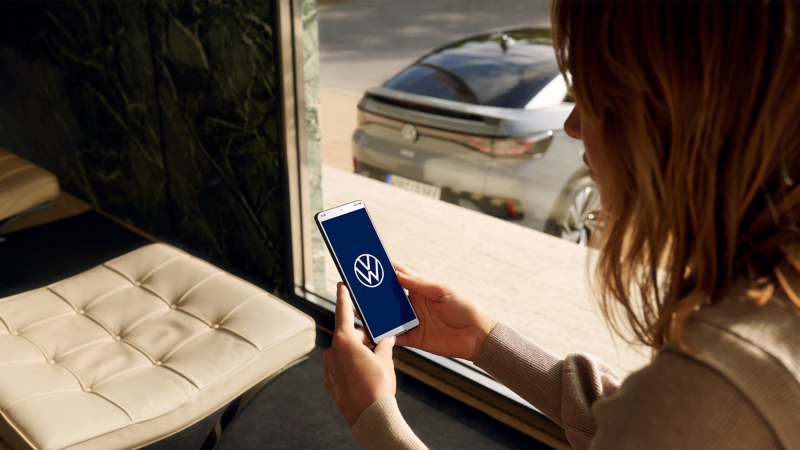 Una mujer mira su teléfono inteligente con el logo de VW – actualización Over-the-Air