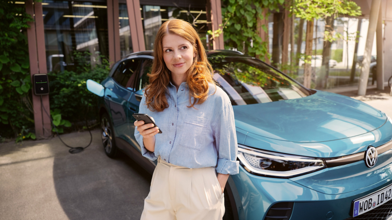 Frau mit Smartphone lächelnd, im Hintergrund VW Auto