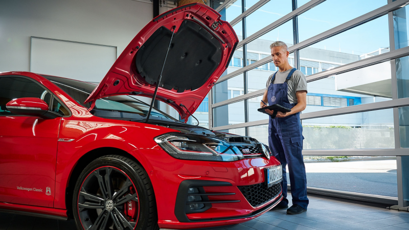 Pracownik serwisu Volkswagena stoi z tabletem przed czerwonym Volkswagenem Golf GTI.