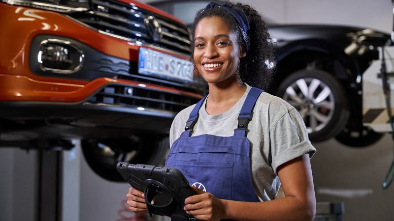 VW-servicemedewerker met een tablet in de hand, met VW T-Cross en VW Touareg op liften in de achtergrond