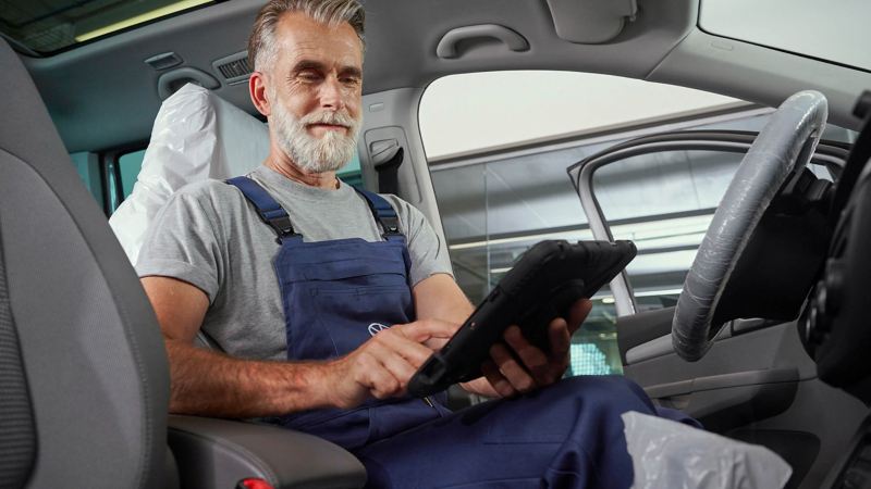 A VW technician using an iPad while sitting in the passenger seat of a VW vehicle. 