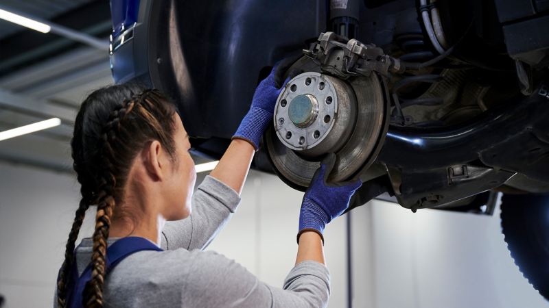 VW Servicemitarbeiterin prüft Bremsscheibe einer VW Bremse – VW Bremsen Service