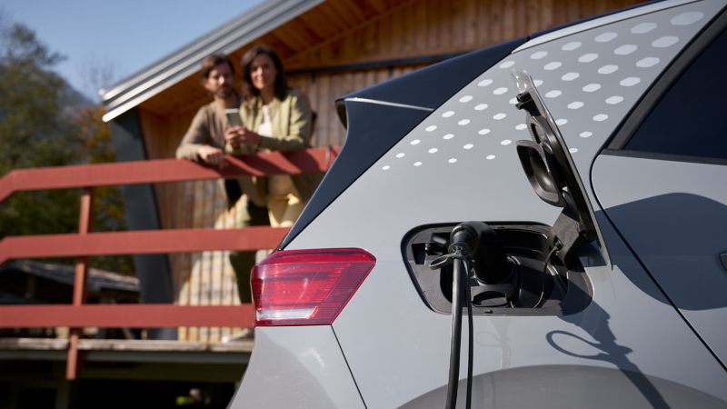 Detailansicht Ladekabel in VW ID. Auto, im Hintergrund ein Paar auf einer Veranda