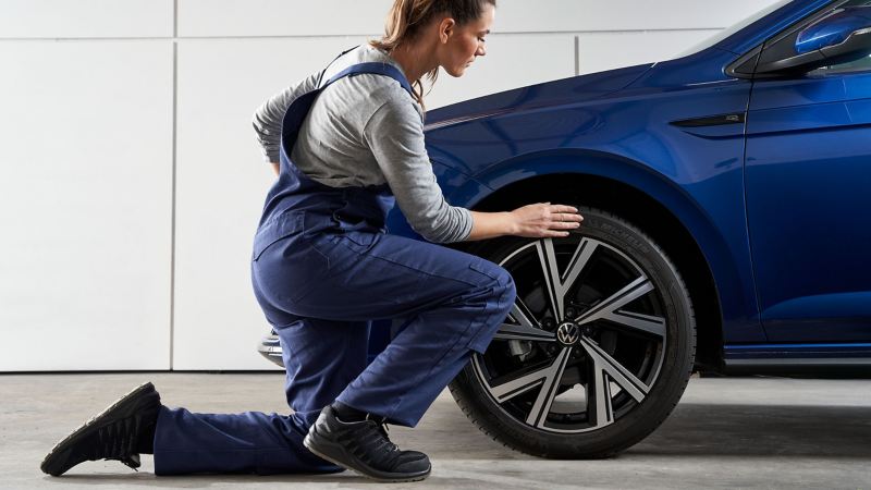 A VW service employee fixes the wheel after the tyre change of a blue VW car